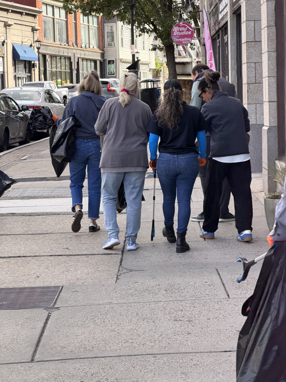 Team members walking a downtown sidewalk with trash grabbers and bags